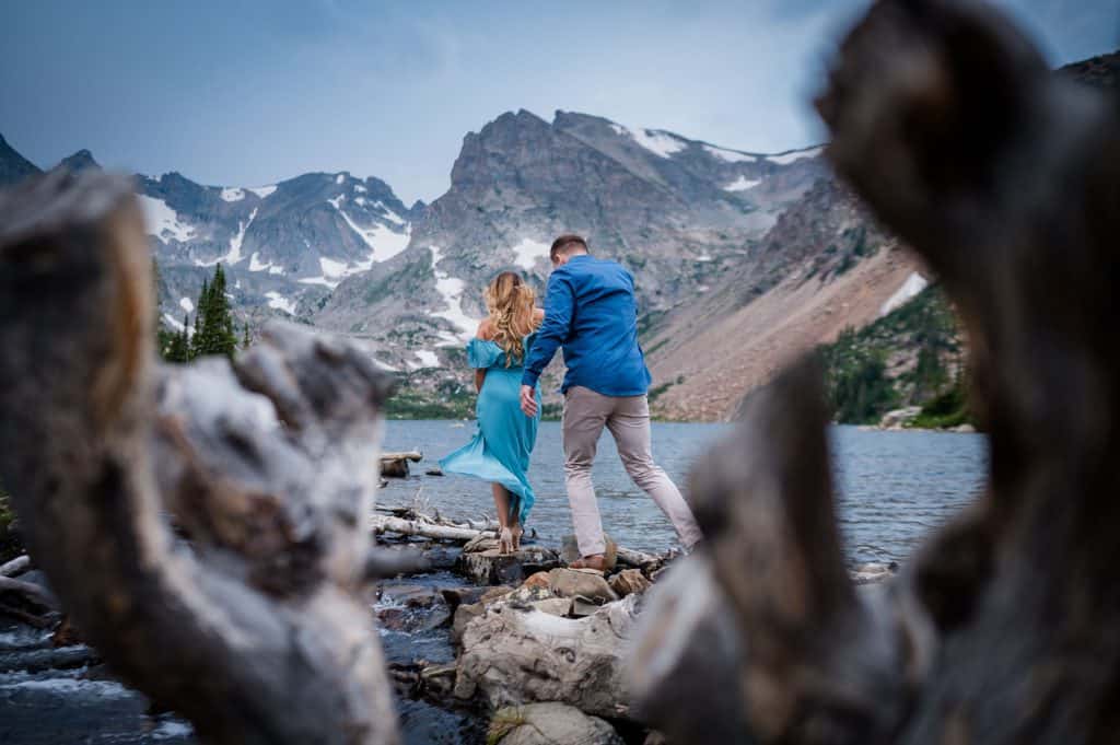 a couple walks across a stream at Lake Isabelle for their adventure engagement session