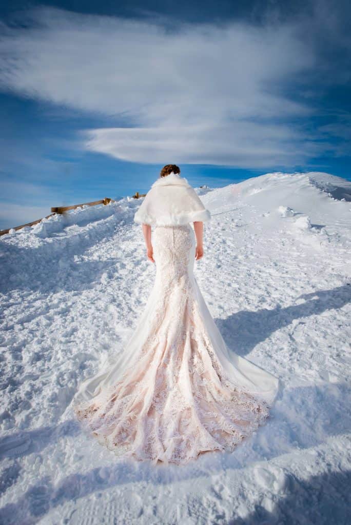 A bride walks up a snowy ridgeline at A-Basin for photos at their snowboarding elopement