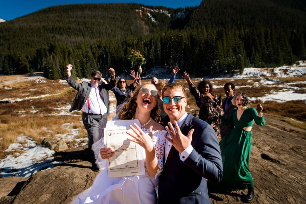 a couple celebrates with their rings, marriage license and family behind them after their hiking elopement in Colorado
