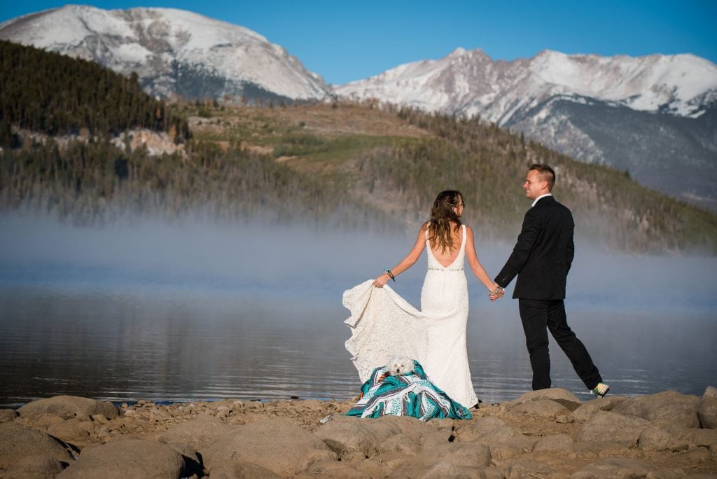 A couple stands at a Dillon Lake Elopement Location with their little dog in Colorado