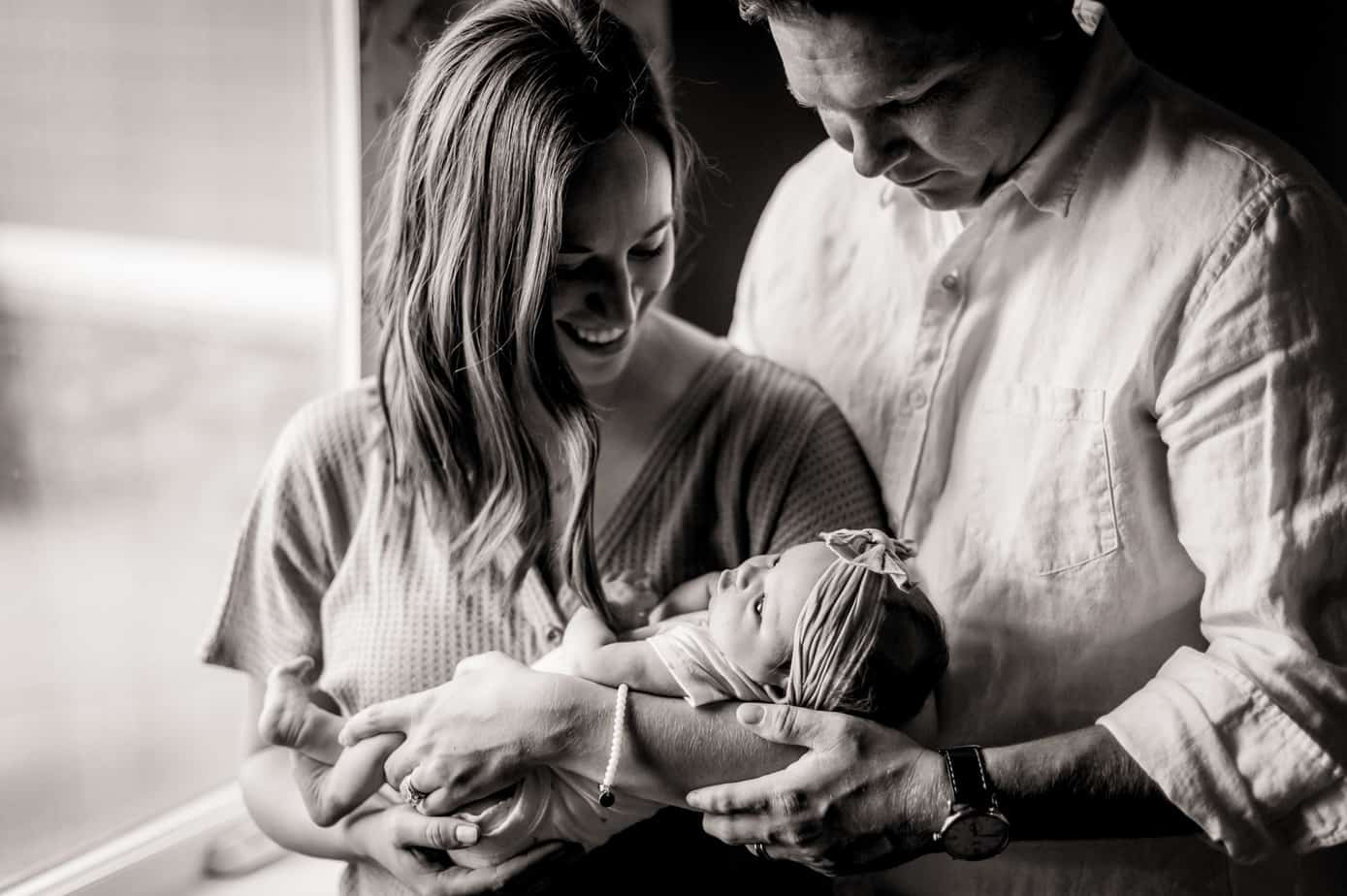 Parents hold their baby in the soft window light of the nursery
