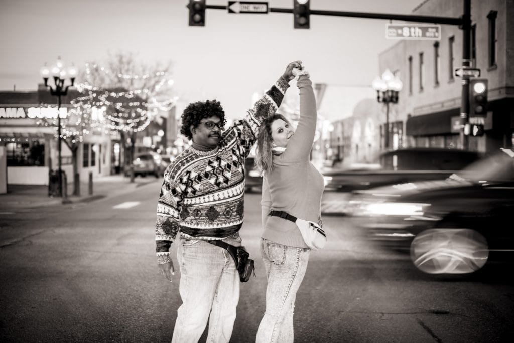 Couple poses together in the streets of Denver in 80s styled clothes for their awkward 80s engagement session