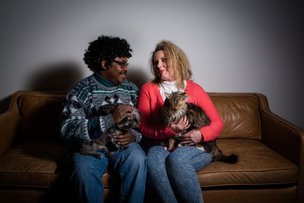 Couple poses with their dog and cat in a photo studio in Denver, Colorado for their 80s styled engagement session
