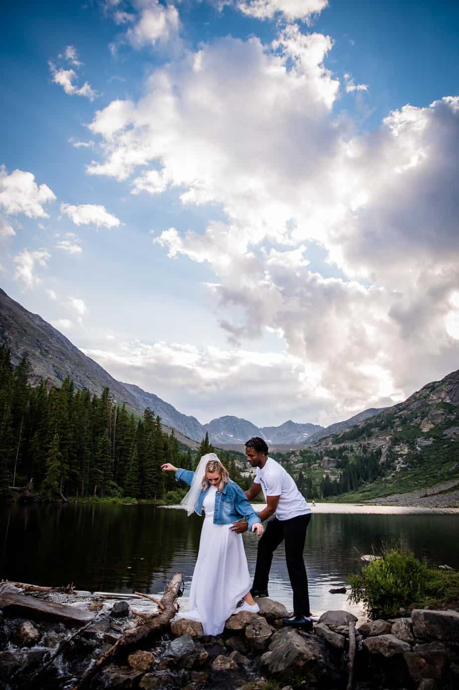 a groom helps his bride cross a stream at blue lakes in Breckenridge after their elopement