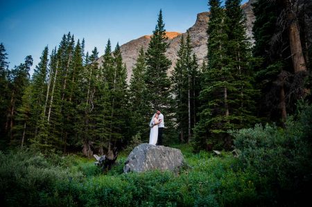 a bride and groom embrace on a big boulder in a field of wildflowers after their elopement in Breckenridge