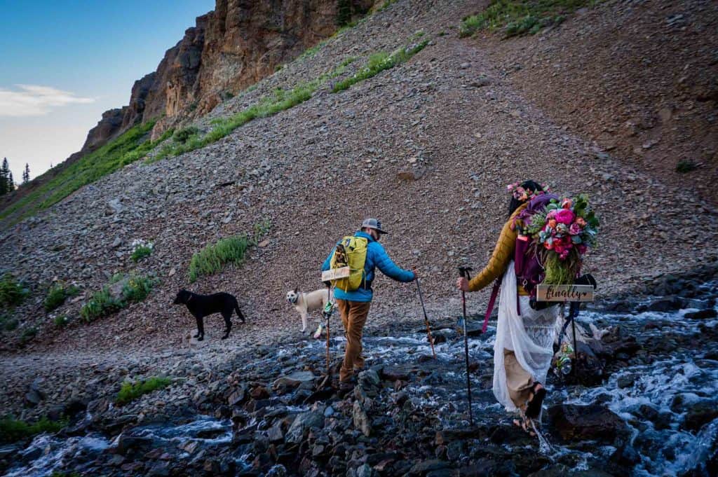 a bride and groom cross a stream after their elopement on top of blue lakes in ridgway, colorado