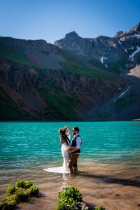 a bride and groom stand in the lower blue lake in Ridgway underneath Sneffels and Dallas Peak