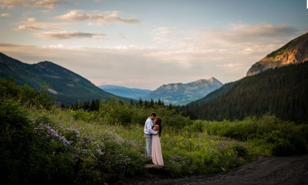 a couple embraces in the wildflowers at sunrise with Mt Crested Butte in the background for their adventure anniversary photography session.