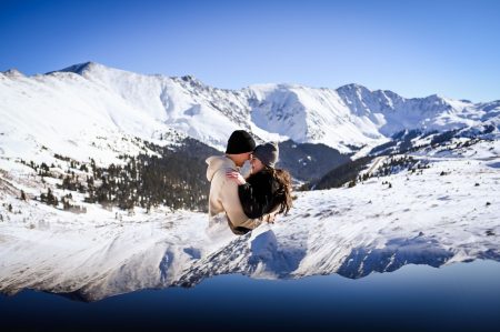 a couple embraces on a snowy mountain top on a sunny colorado day