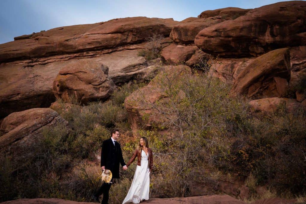 a couple walks hand in hand after their elopement at Red Rocks Park in Morrison, Colorado