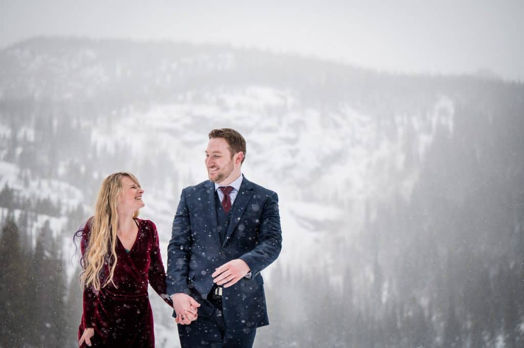 A couple walks hand in hand in a blizzard at their Colorado adventure engagement photography in RMNP