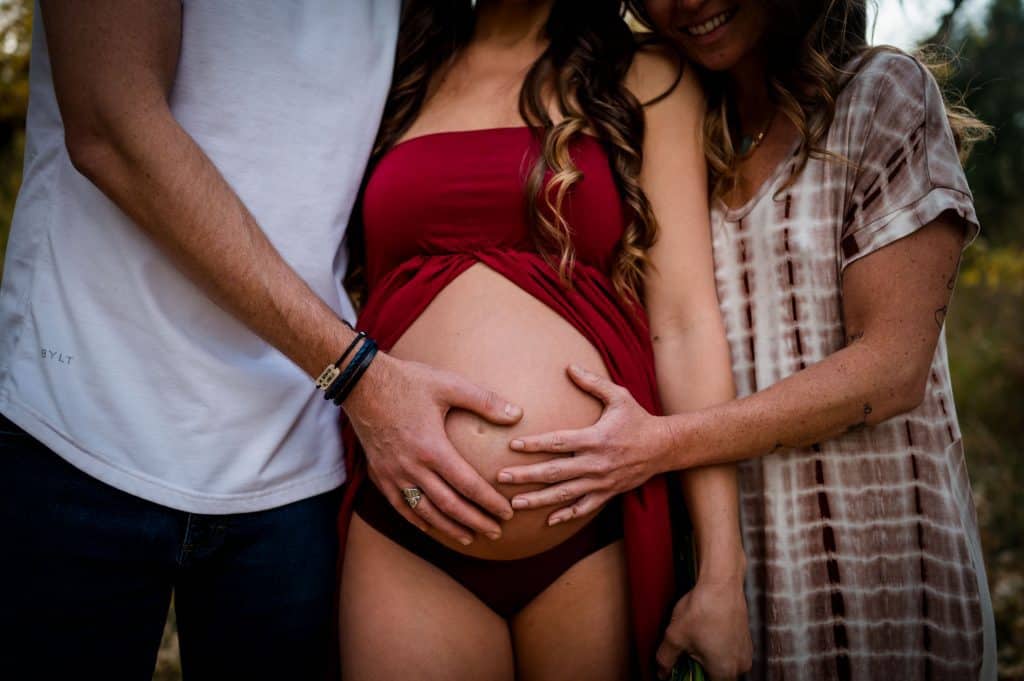 a pregnant throuple holds their baby bump at their Colorado maternity photography