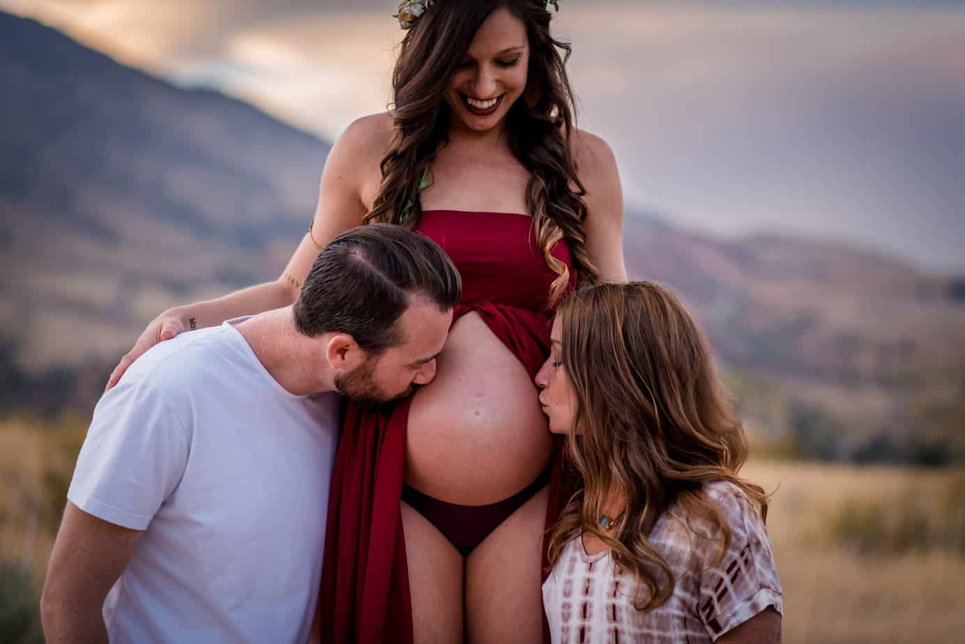 a throuple embraces their pregnant belly in Morrison, Colorado near Red Rocks for their maternity photos
