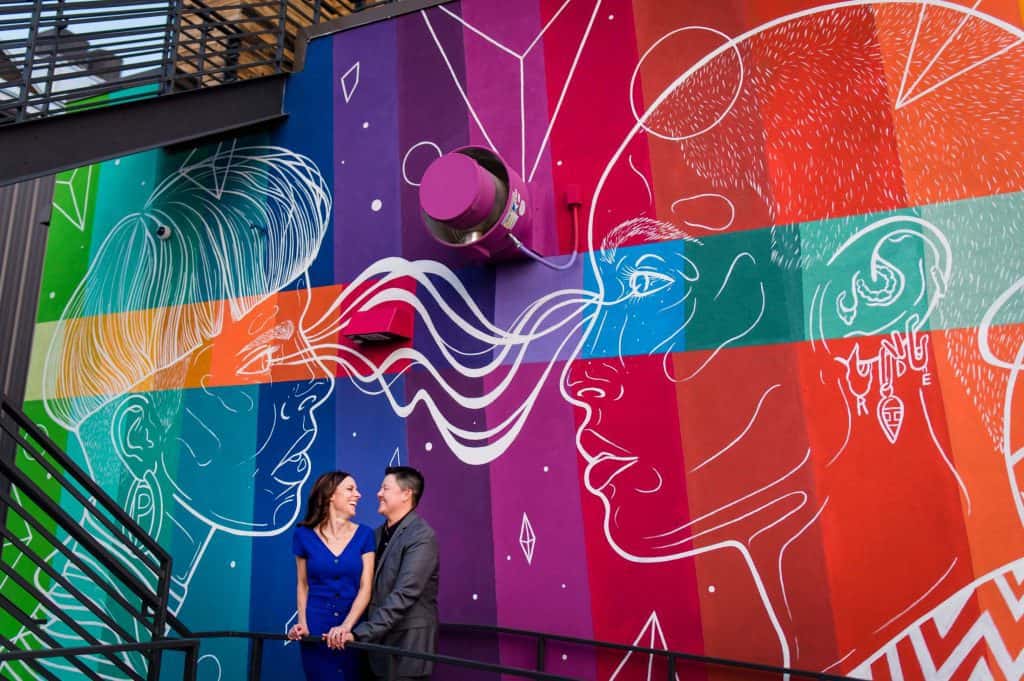 a couple stands in front of a rainbow portrait mural in RiNo near downtown denver for their engagement photos