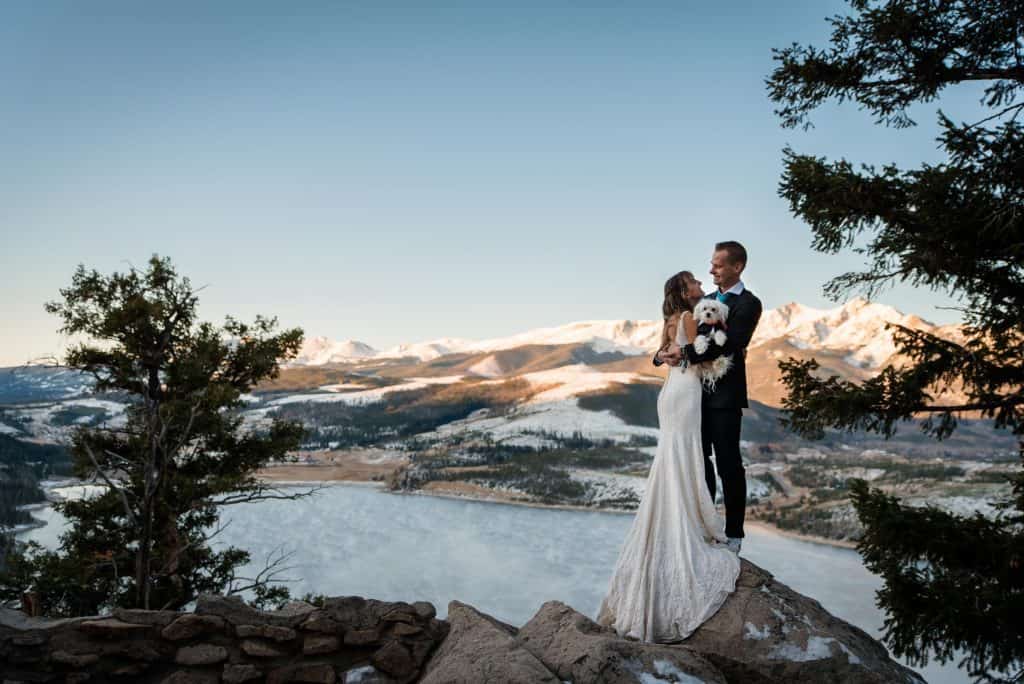a couple snuggles with their dog over Dillon Lake in Summit County, Colorado for a sunrise elopement shoot in 4 degree temps