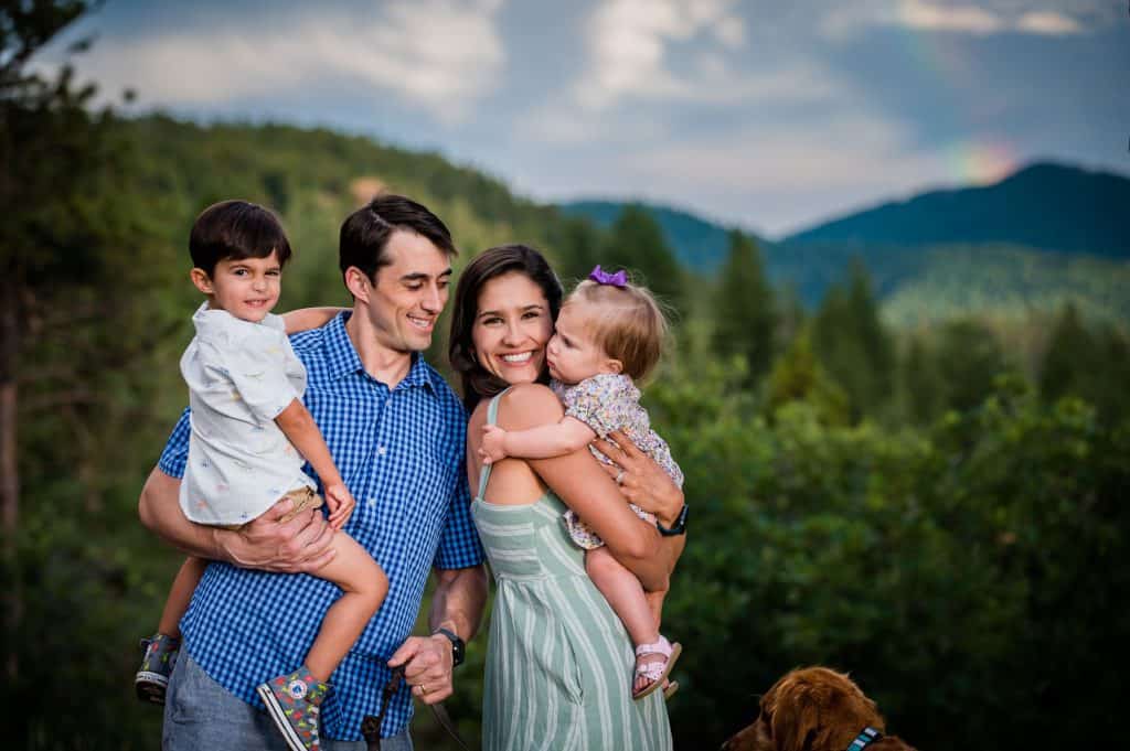 a family and their dog huddle in the mountains together under a rainbow in Colorado