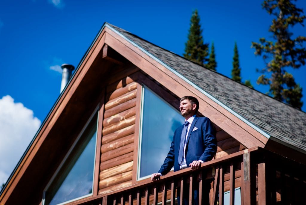 a groom stands on the balcony of their airbnb in Breckenridge while the bride gets ready