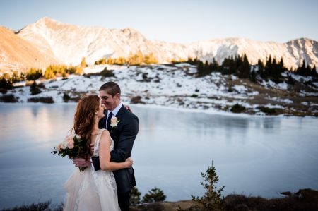 a couple embraces above a frozen alpine lake in the mountains at their elopement in Colorado