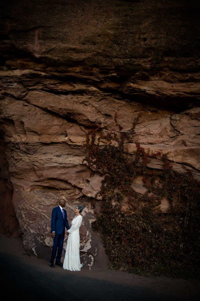 An interracial couple stands in front of a red rock wall for photos celebrating their 40th vow renewal in Morrison, Colorado