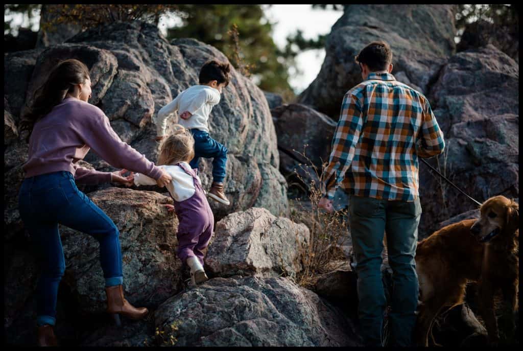 A mom, dad, and two kids climb boulders with their dog at their family photography adventure in Colorado