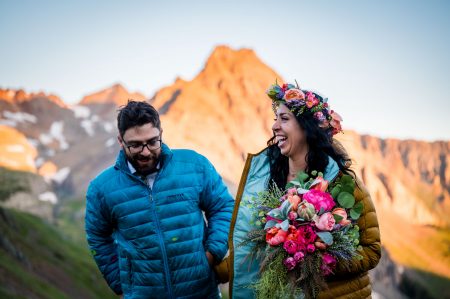 a couple puts on their puffeys to warm up after their backpacking elopement at sunrise with Dallas Peak and the San Juan Mountains in the background