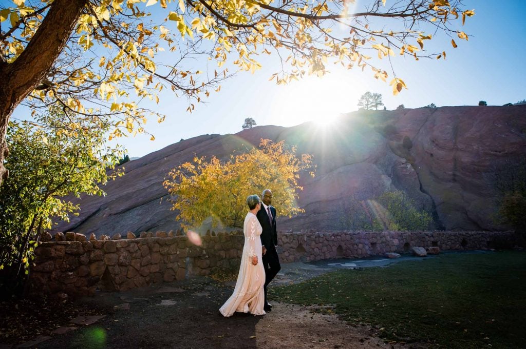 a couple walks hand in hand in front of red rocks amphitheater for their 40th anniversary vow renewal photos