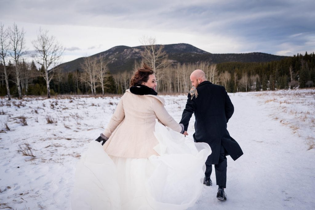 a couple runs down a snowy trail at their winter elopement in Colorado