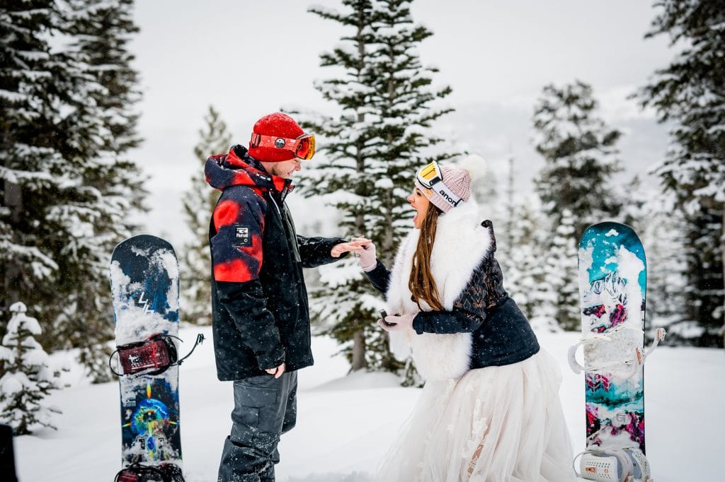 a couple exchanges rings at their mountainside elopement ceremony on their snowboards at Breckenridge Resort