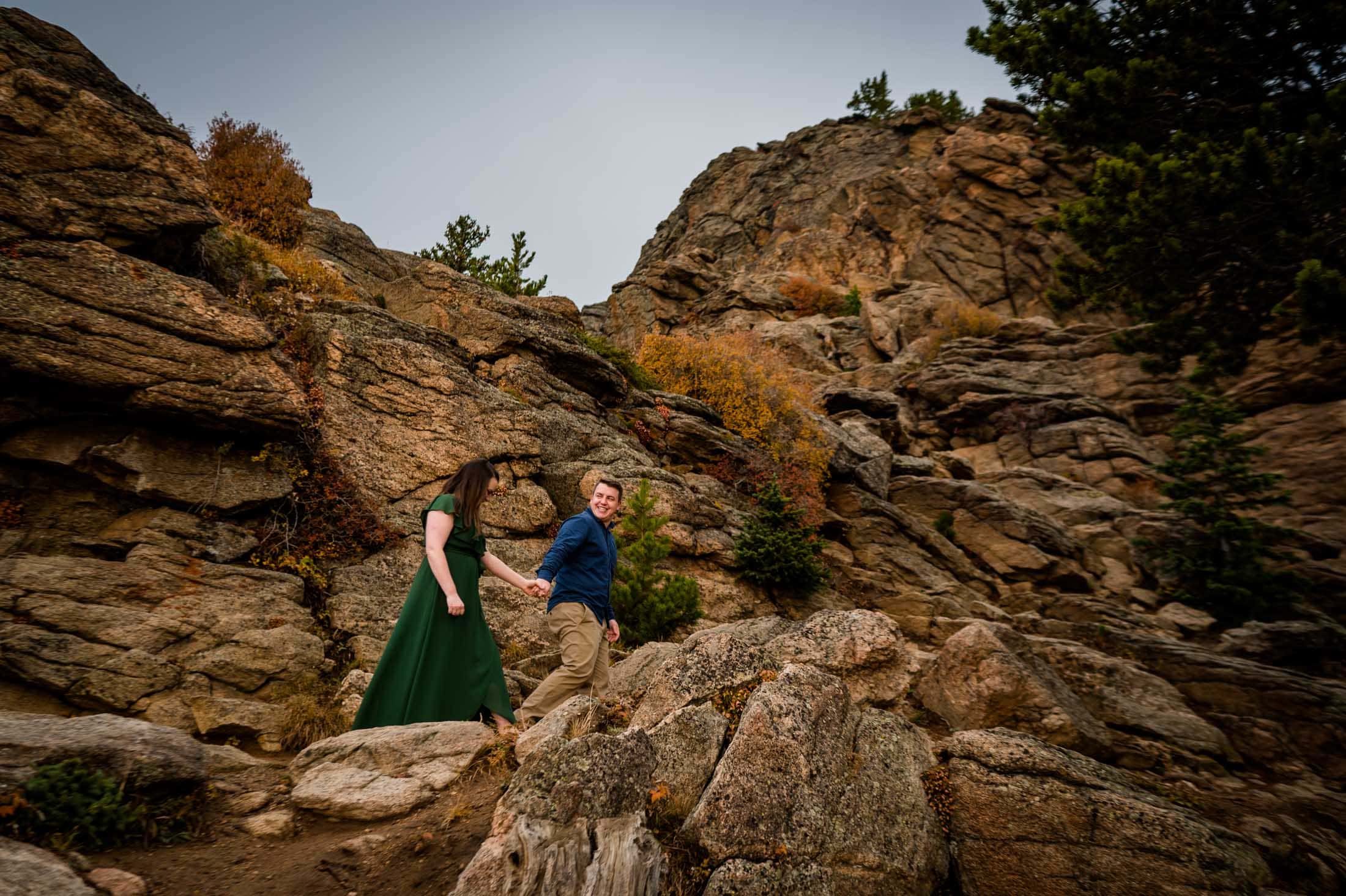 an engaged couple walks hand in hand in the mountains of colorado