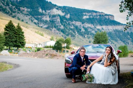 a couple poses in front of their red convertible getaway car on their wedding day in vail, colorado