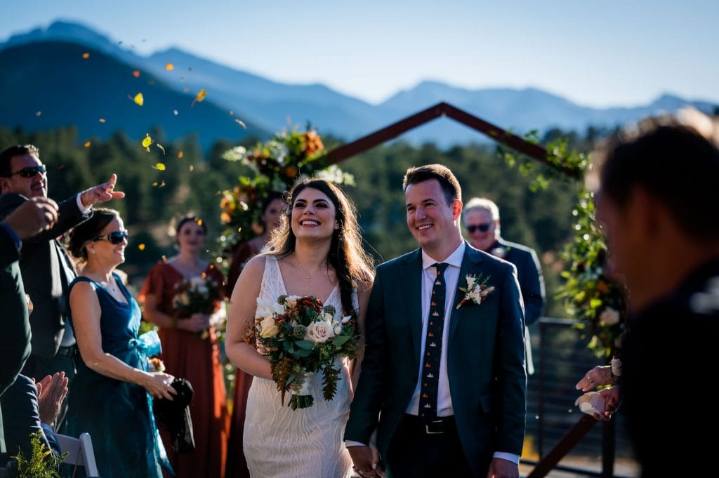 a happy couple walks back down the aisle while guests through golden leaves after their Fall wedding at Skyview at Fall River Village in Estes Park, Colorado