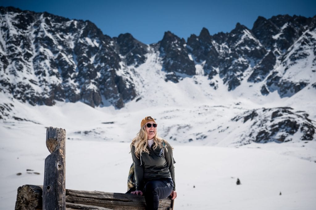 A girl sits on old mining ruins under snowy, jagged mountain peaks at a colorado adventure hike near Mayflower Gulch