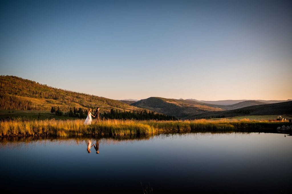 a couple walks hand in hand after their wedding at Strawberry Creek Ranch during sunset against a perfectly calm, reflective lake.