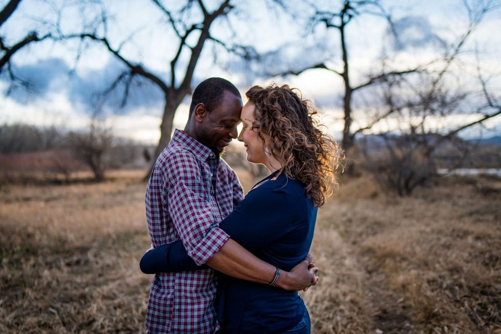 an interracial couples snuggles in the warm golden sunset light at their engagement session in the mountains of Colorado