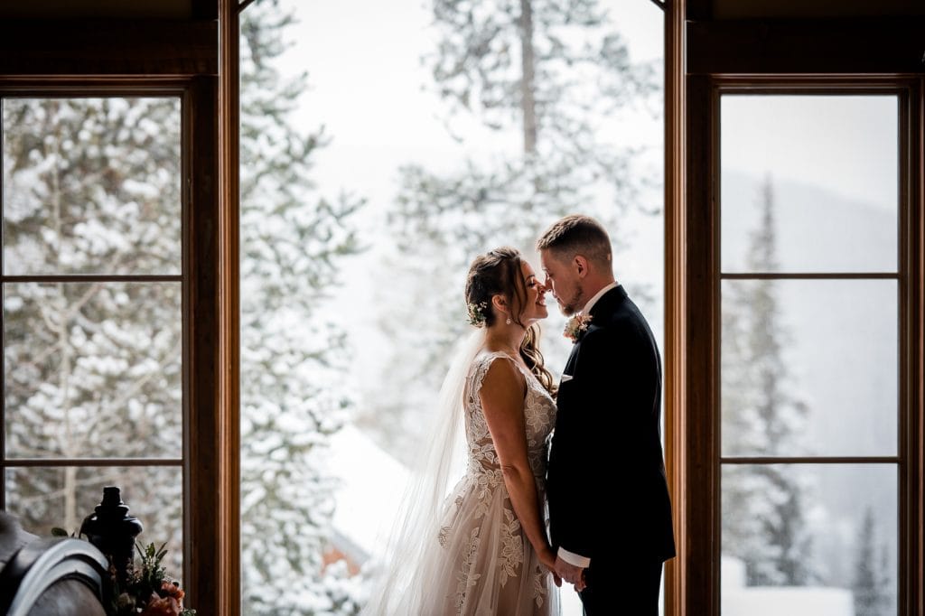 a couple smooshes noses on their elopement day in front of a big window with a white out snow storm in the background at their cabin in Breckenridge