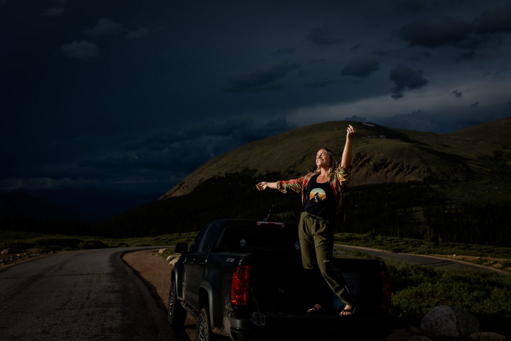 adventure photographer Nat Moore dances in the sun in the back of her truck up a mountain pass in Colorado
