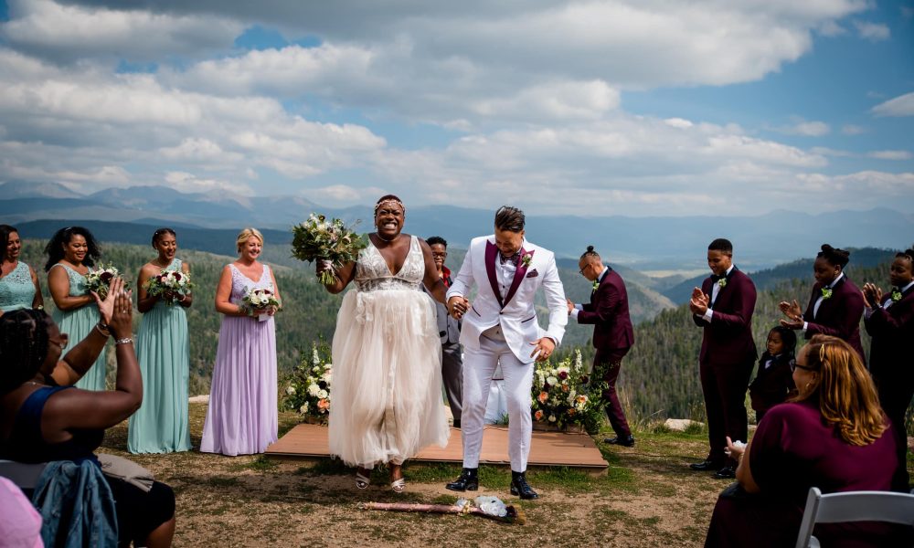 a couple jumps the broom after their wedding on top of granby ranch in colorado mountains