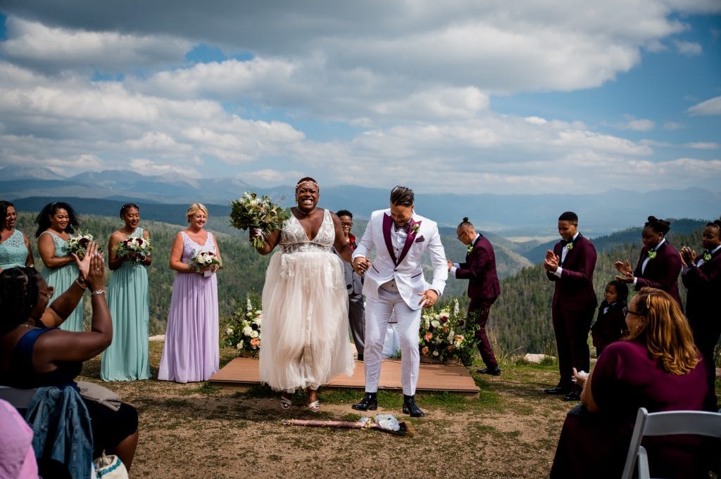 a couple jumps the broom after their wedding on top of granby ranch in colorado mountains