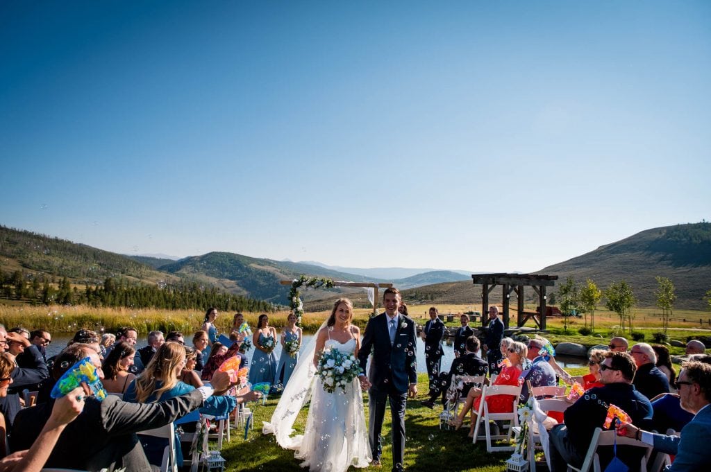 A couple walks back down the aisle with a bubble exit after their ceremony at Strawberry Creek Ranch near Granby, Colorado