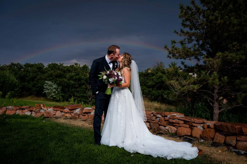 a couple kisses under a rainbow after having rain at their wedding ceremony at the arrowhead golf club in Colorado