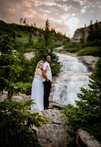 a couple snuggles in front of a waterfall at sunset at their adventure elopement in Breckenridge