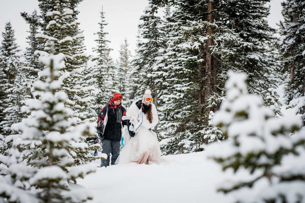 a snowboarding elopement walks out of the snowy trees onto a run at Breckenridge after their vows