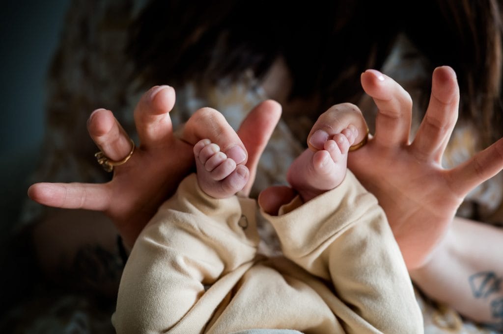 a momma holds her newborn baby's time curled up toes at their in home newborn lifestyle photography session in Colorado