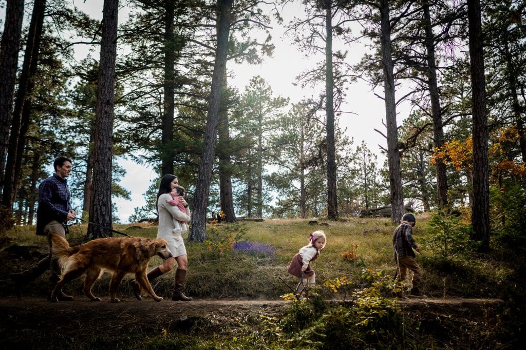 a family marches through the woods on a trail in Colorado for their family photography session