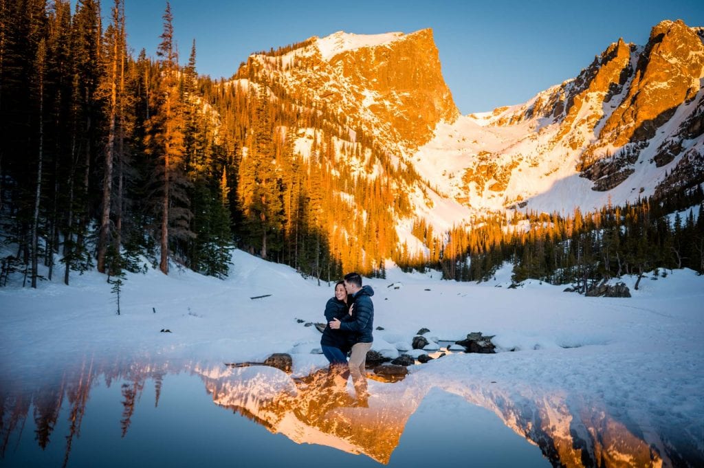 a couple snuggles under a winter sunrise at Dream Lake at their colorado winter adventure proposal in Rocky Mountain National Park