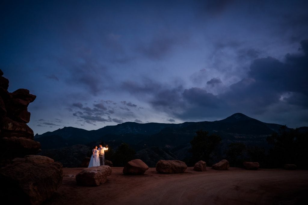 a couple stands together under the light of a lantern at blue hour in their Garden of the Gods Adventure Elopement in Colorado Springs