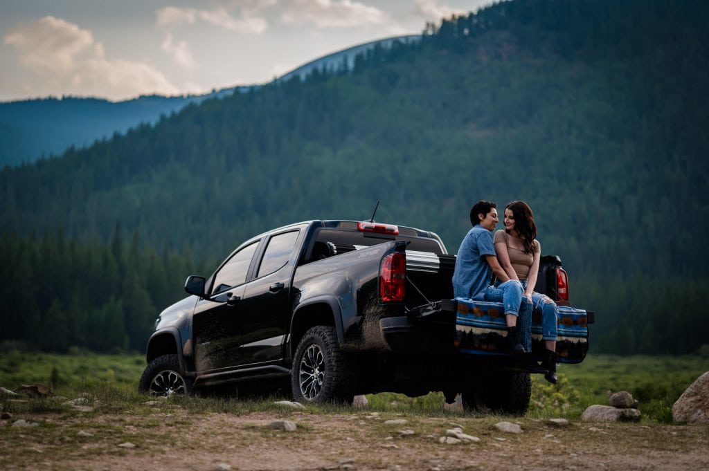 a couple relaxes in the back of their 4x4 on the way to their backcounty elopeent