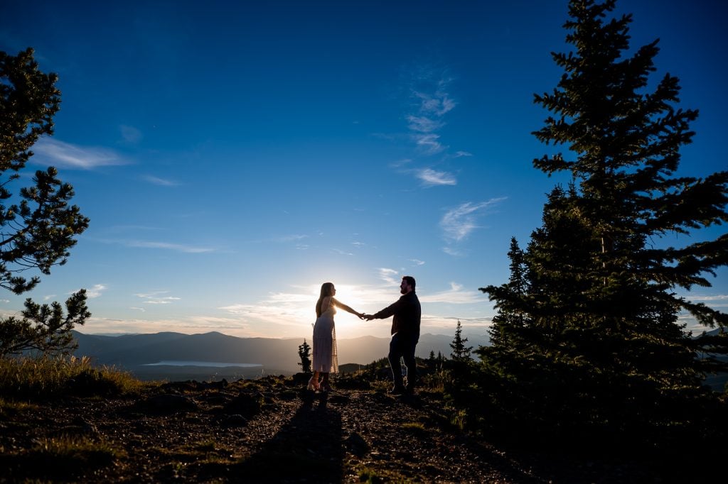 a couple stands hand in hand in the last light of day at their mountain top engagement session near Buena Vista, Colorado