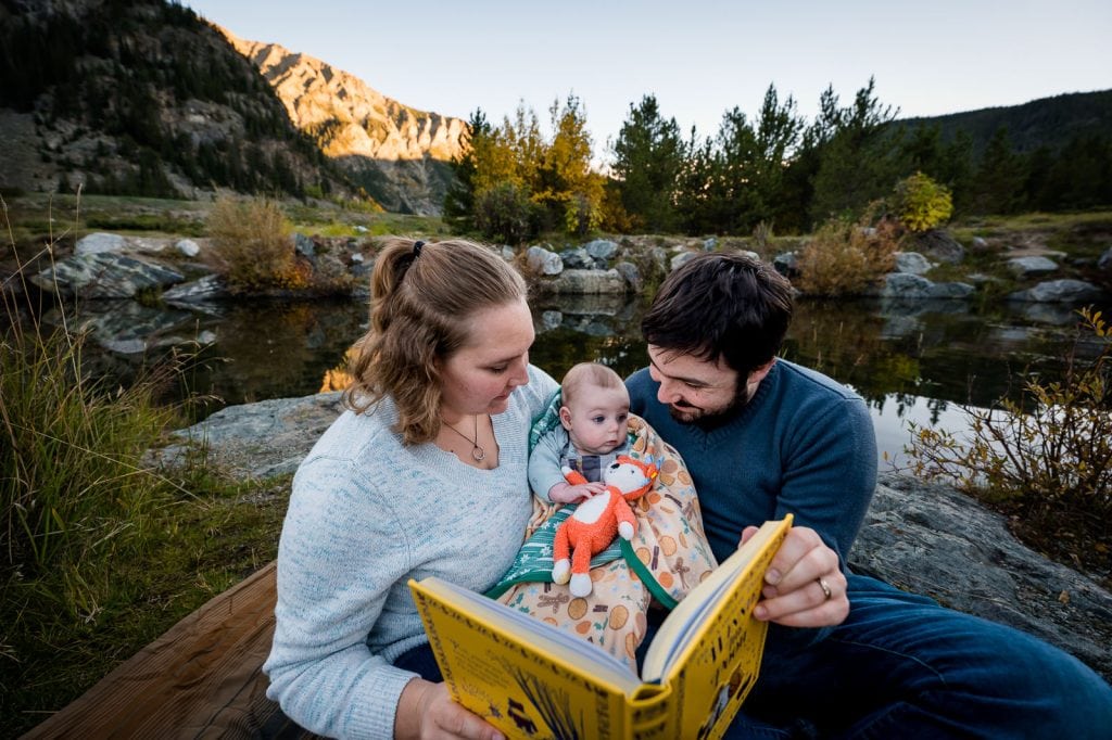 parents read their favorite childhood book to their new daughter as they snuggle in the mountains